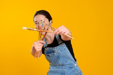 Woman with paintbrushes on yellow background. Young artist