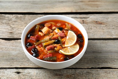 Photo of Meat solyanka soup with sausages, olives and vegetables in bowl on wooden table