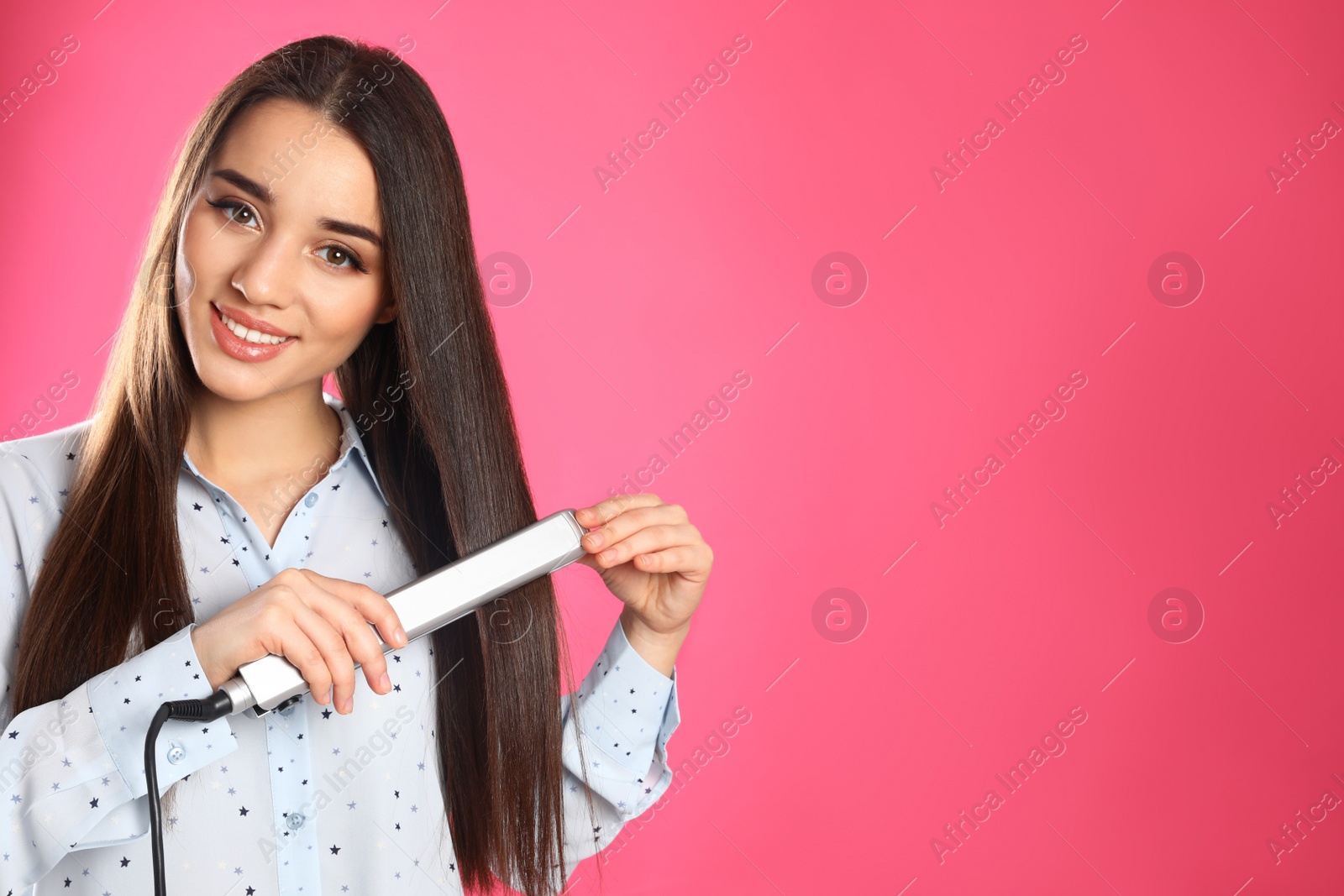 Photo of Happy woman using hair iron on color background. Space for text