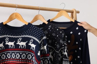 Photo of Woman picking Christmas sweater from rack near white wall, closeup