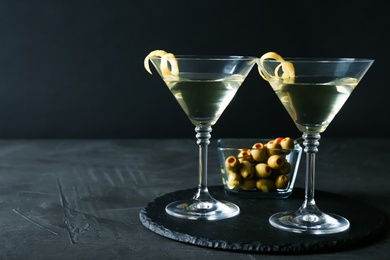 Photo of Glasses of Lemon Drop Martini cocktail with zest on grey table against black background. Space for text
