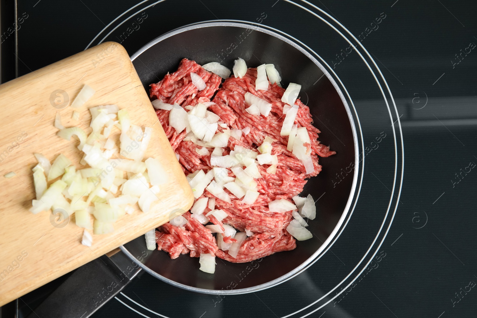 Photo of Adding chopped onion on frying pan with raw minced meat, top view