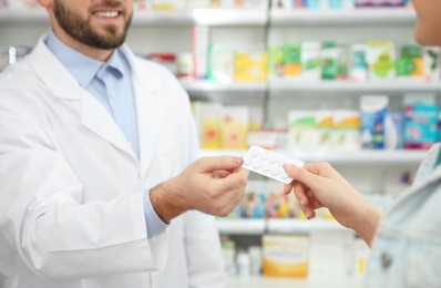 Photo of Professional pharmacist giving pills to customer in modern drugstore, closeup
