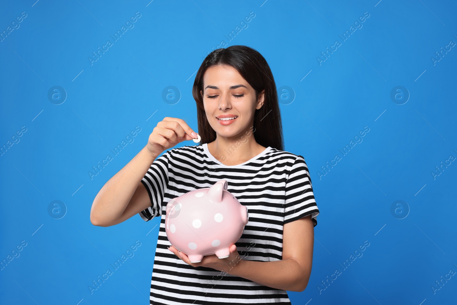 Photo of Young woman putting coin into piggy bank on light blue background