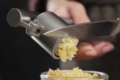 Photo of Woman squeezing garlic with press on blurred background, closeup