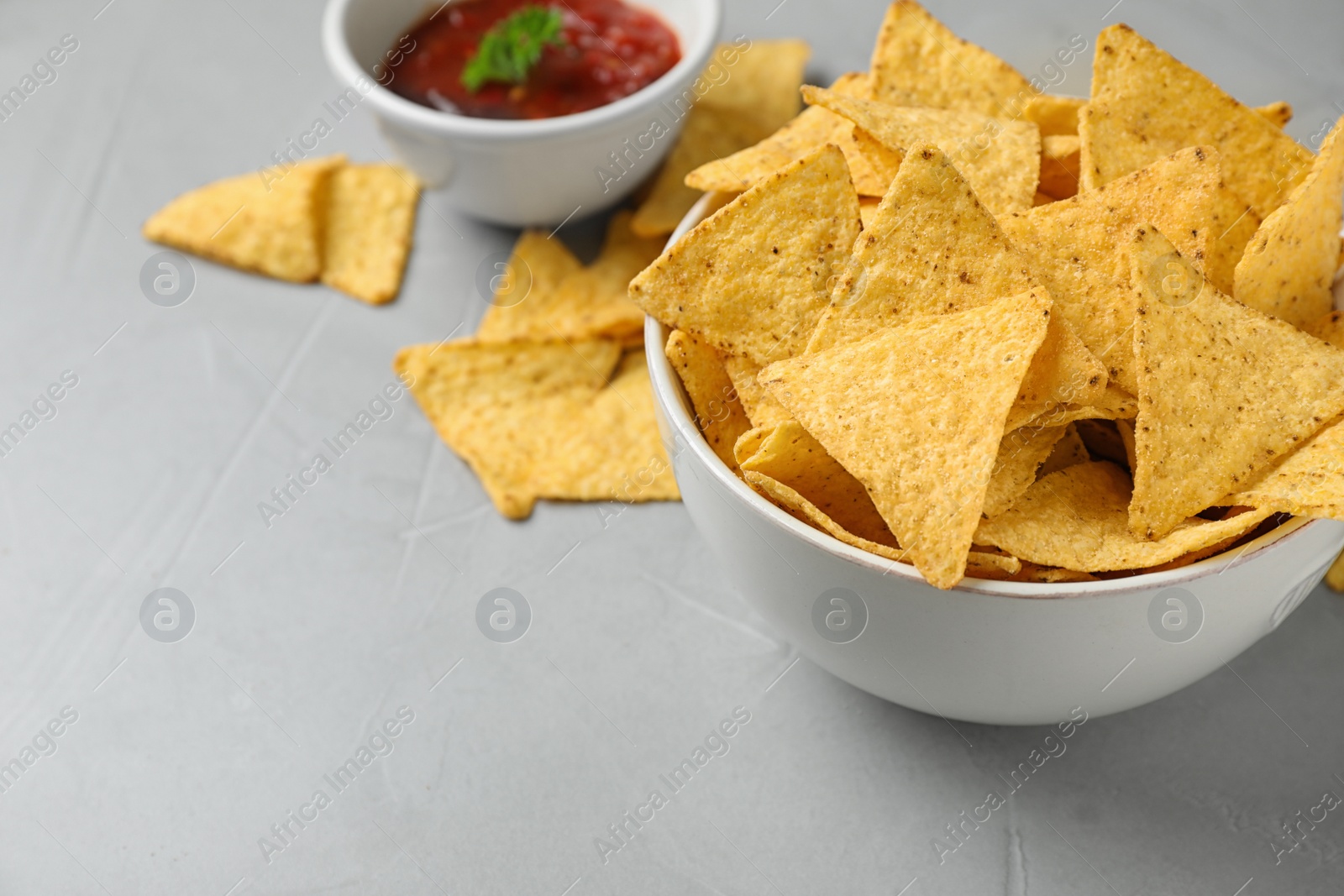 Photo of Bowl with tasty Mexican nachos chips and sauce on grey table, space for text