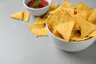 Bowl with tasty Mexican nachos chips and sauce on grey table, space for text