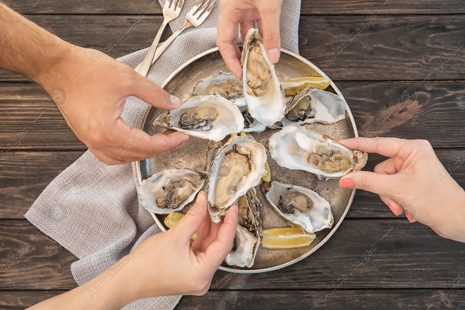 Photo of Top view of people with fresh oysters at table, focus on hands