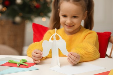Photo of Cute little girl with paper angel for Saint Nicholas day at home, focus on hands