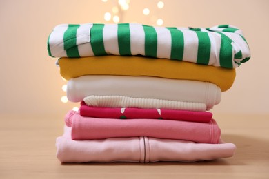 Photo of Stack of folded clothes on wooden table against beige background