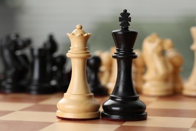 Photo of White wooden queen and black king on chess board, closeup