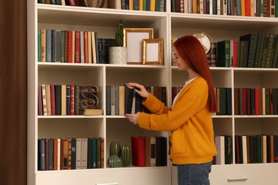 Photo of Beautiful young woman taking book from shelf in home library