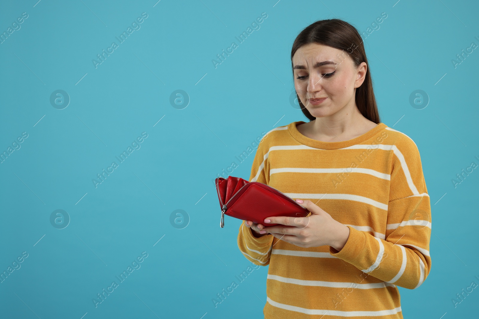 Photo of Sad woman with empty wallet on light blue background, space for text