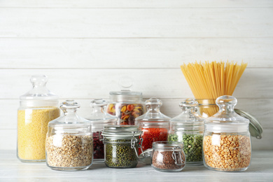 Glass jars with different types of groats and pasta on white wooden table