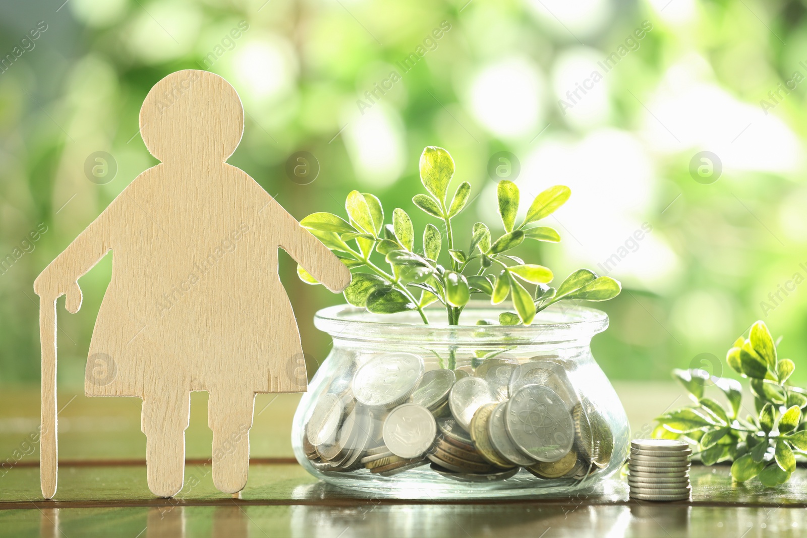 Photo of Pension savings. Figure of senior woman, coins and green twigs on wooden table outdoors