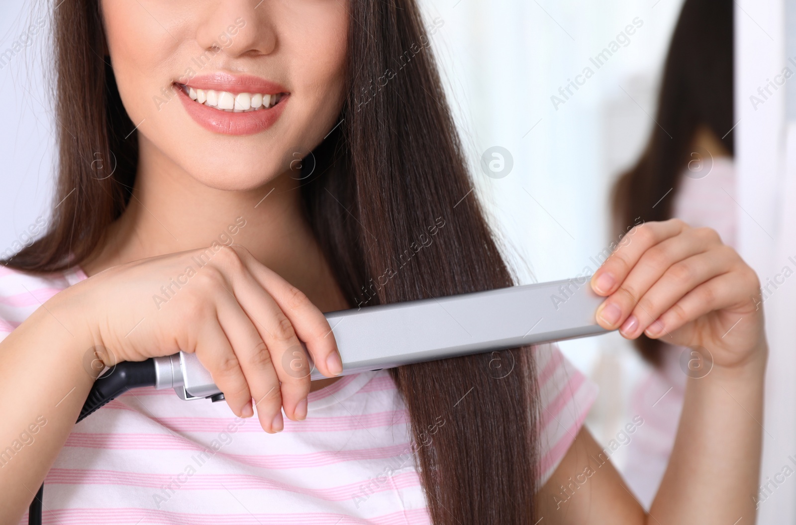 Photo of Happy woman using hair iron on blurred background, closeup