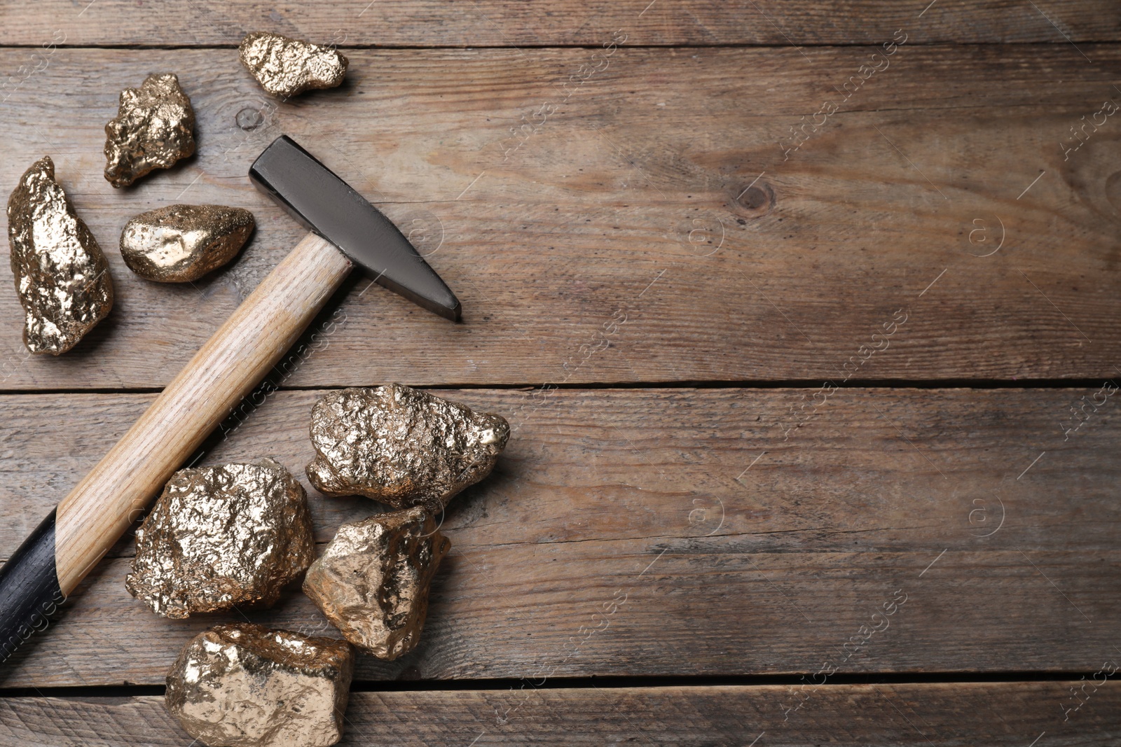 Photo of Pile of gold nuggets and hammer on wooden table, flat lay. Space for text