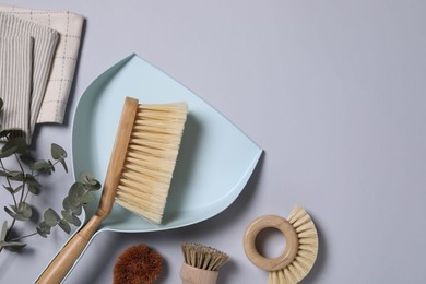 Photo of Cleaning brushes, scoop, towel and eucalyptus leaves on grey background, flat lay. Space for text