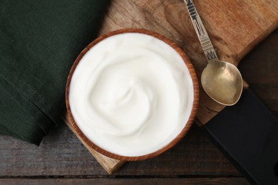 Photo of Delicious natural yogurt in bowl and spoon on wooden table, top view