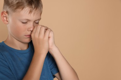 Photo of Boy with clasped hands praying on beige background, space for text