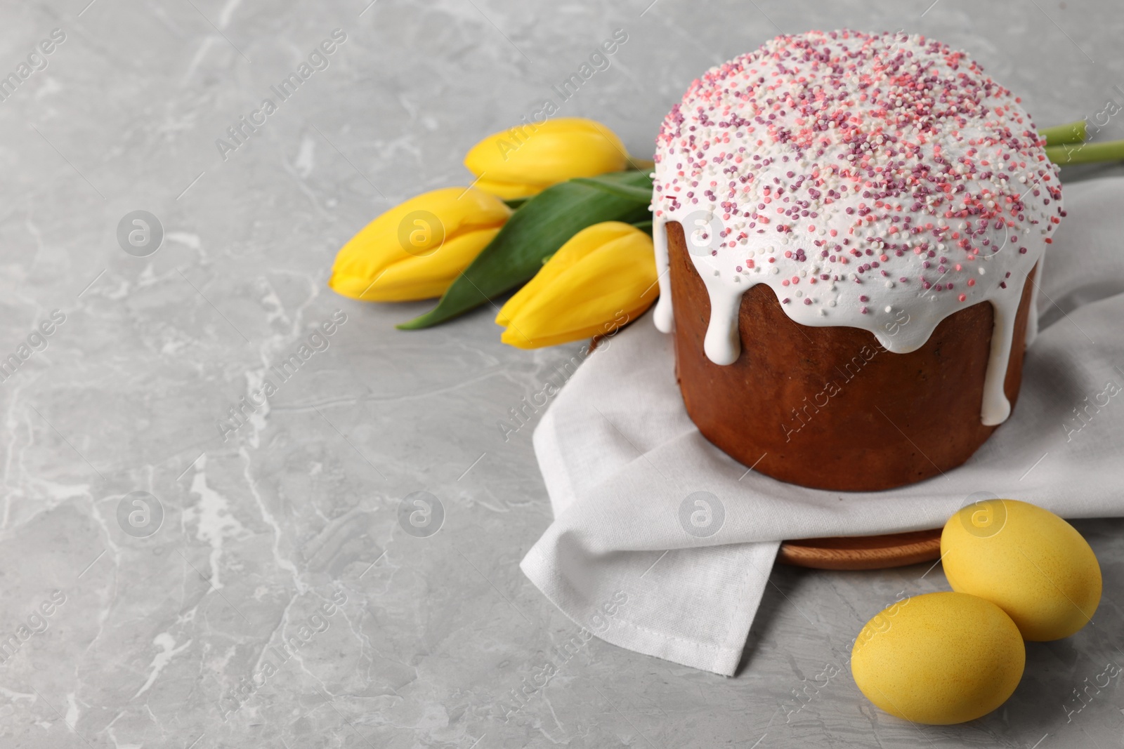 Photo of Tasty Easter cake, decorated eggs and flowers on grey table. Space for text