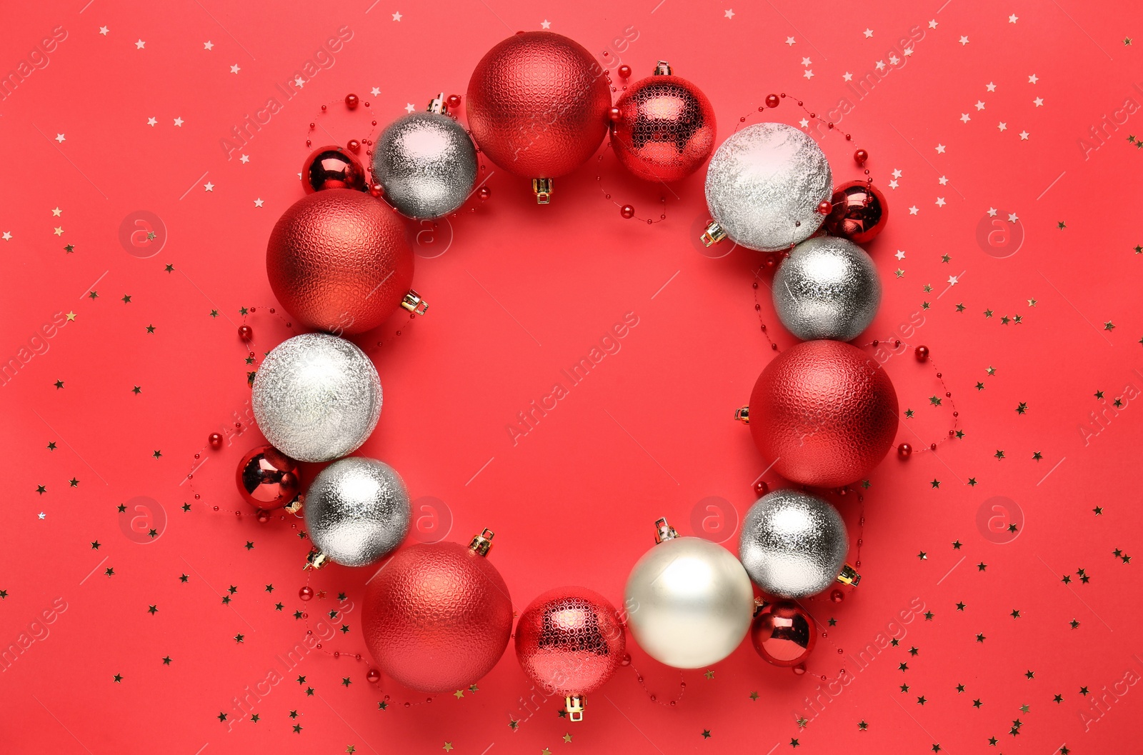 Photo of Beautiful festive wreath made of color Christmas balls on red background, top view