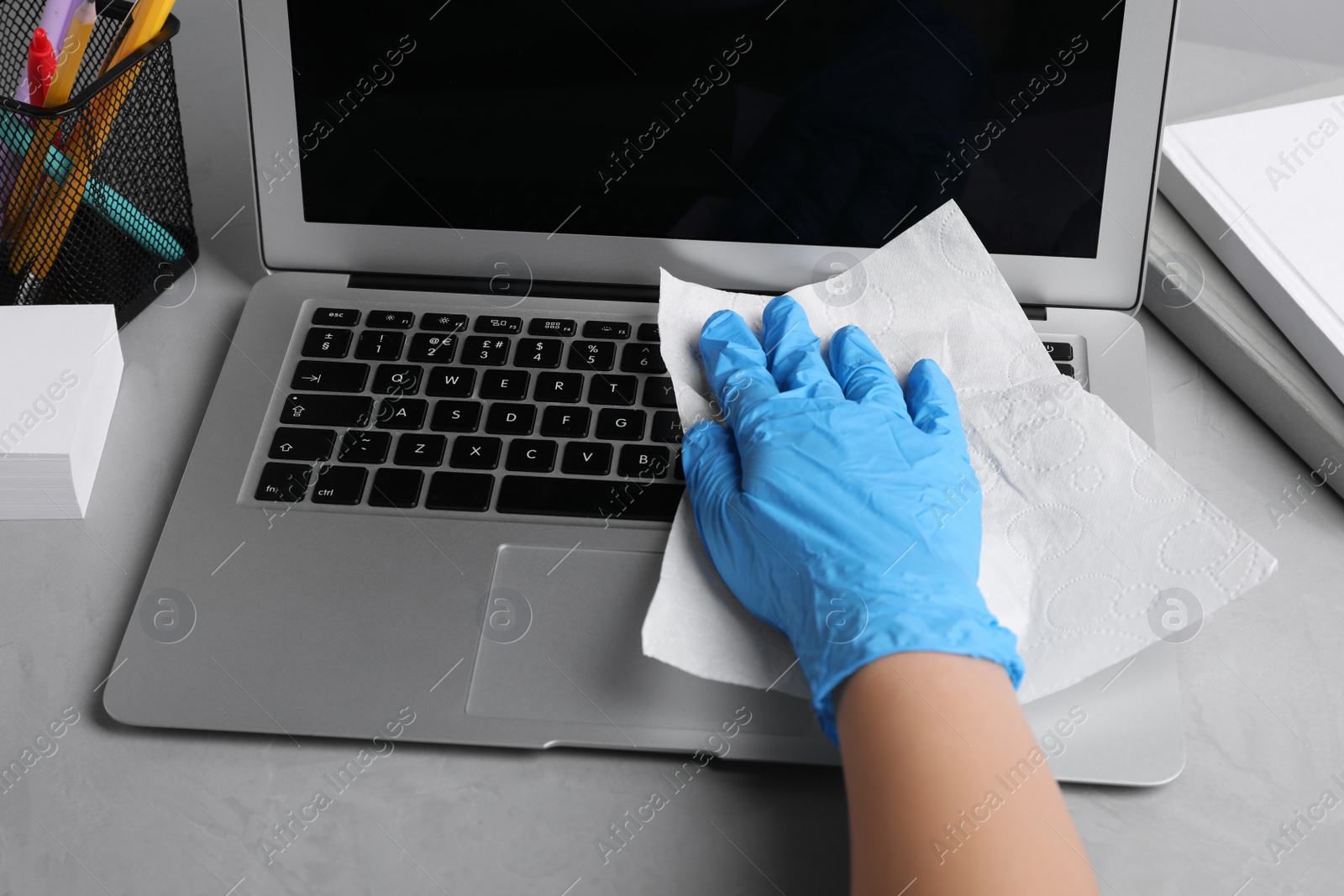 Photo of Woman wiping laptop with paper towel at gray table, closeup