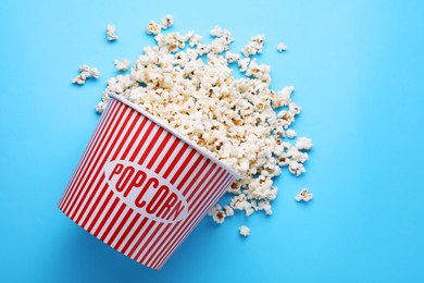 Photo of Overturned paper bucket with delicious popcorn on light blue background, flat lay
