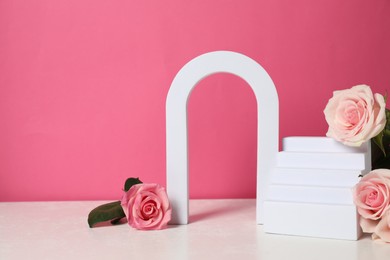 Photo of Stylish presentation for product. Geometric figures and beautiful roses on light table against pink background, space for text