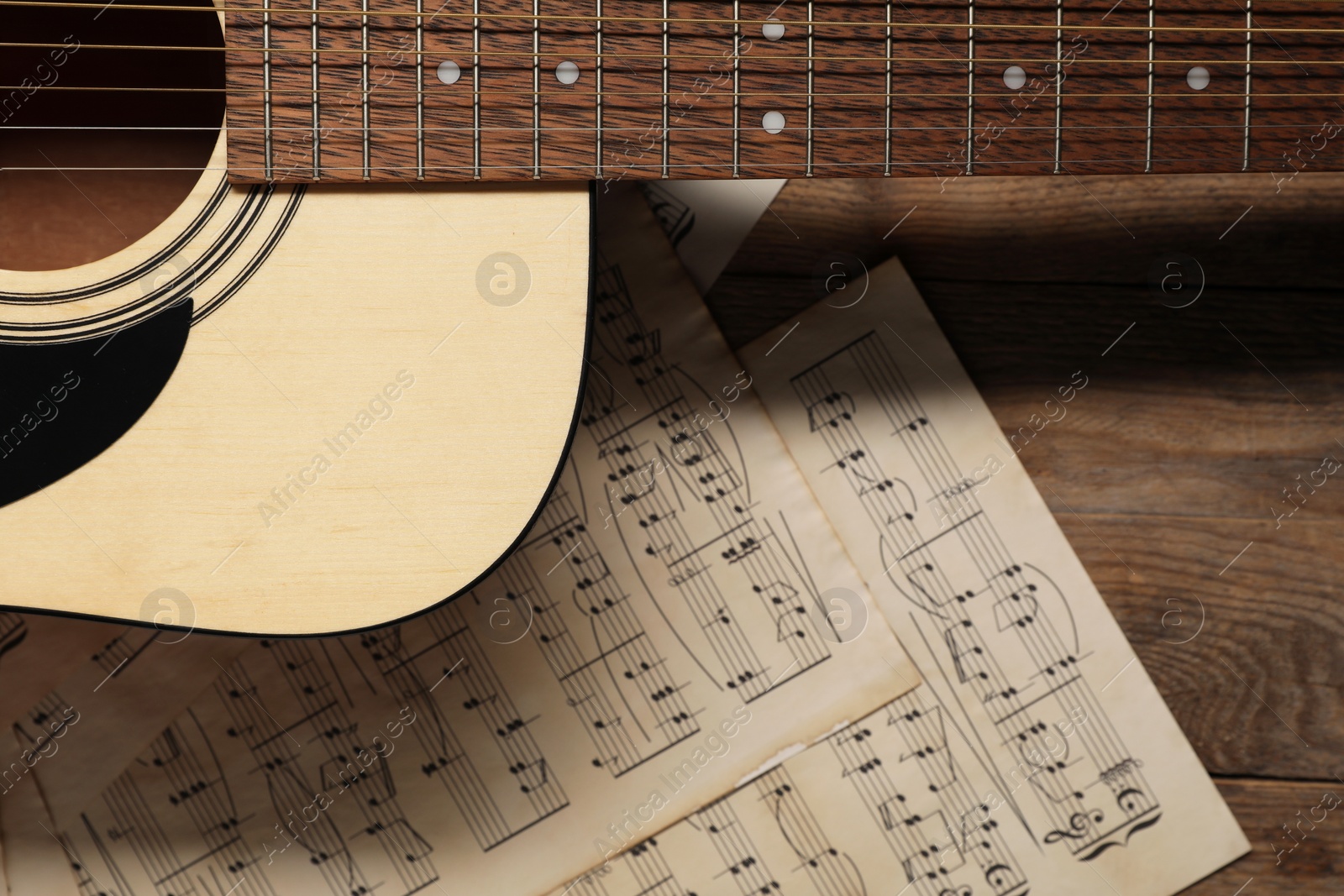 Photo of Paper sheets with music notes and acoustic guitar on wooden table, top view