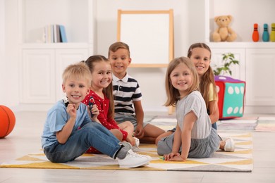Photo of Group of cute little children with finger toys for puppet show on bright rug in kindergarten. Playtime activities