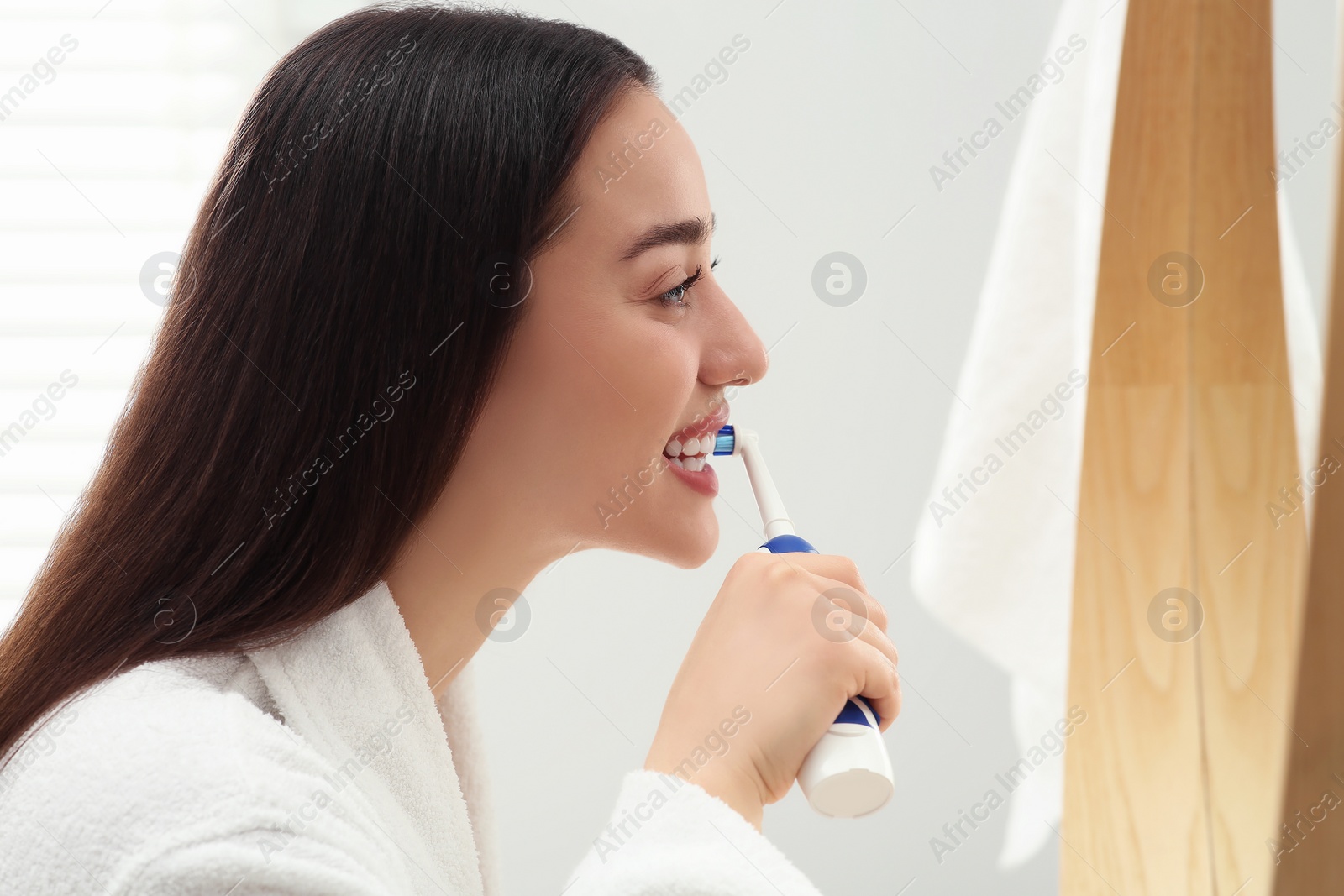 Photo of Young woman brushing her teeth with electric toothbrush near mirror in bathroom