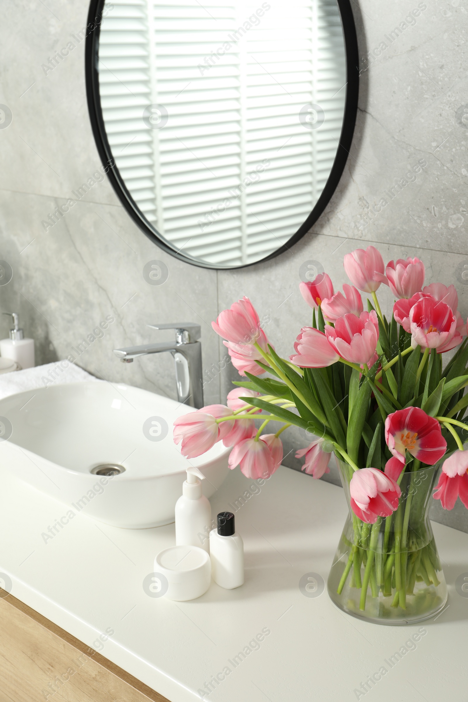 Photo of Vase with beautiful pink tulips and toiletries near sink in bathroom