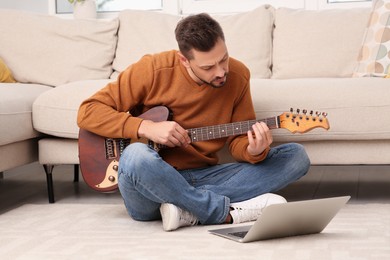 Photo of Man learning to play guitar with online music course at home. Time for hobby