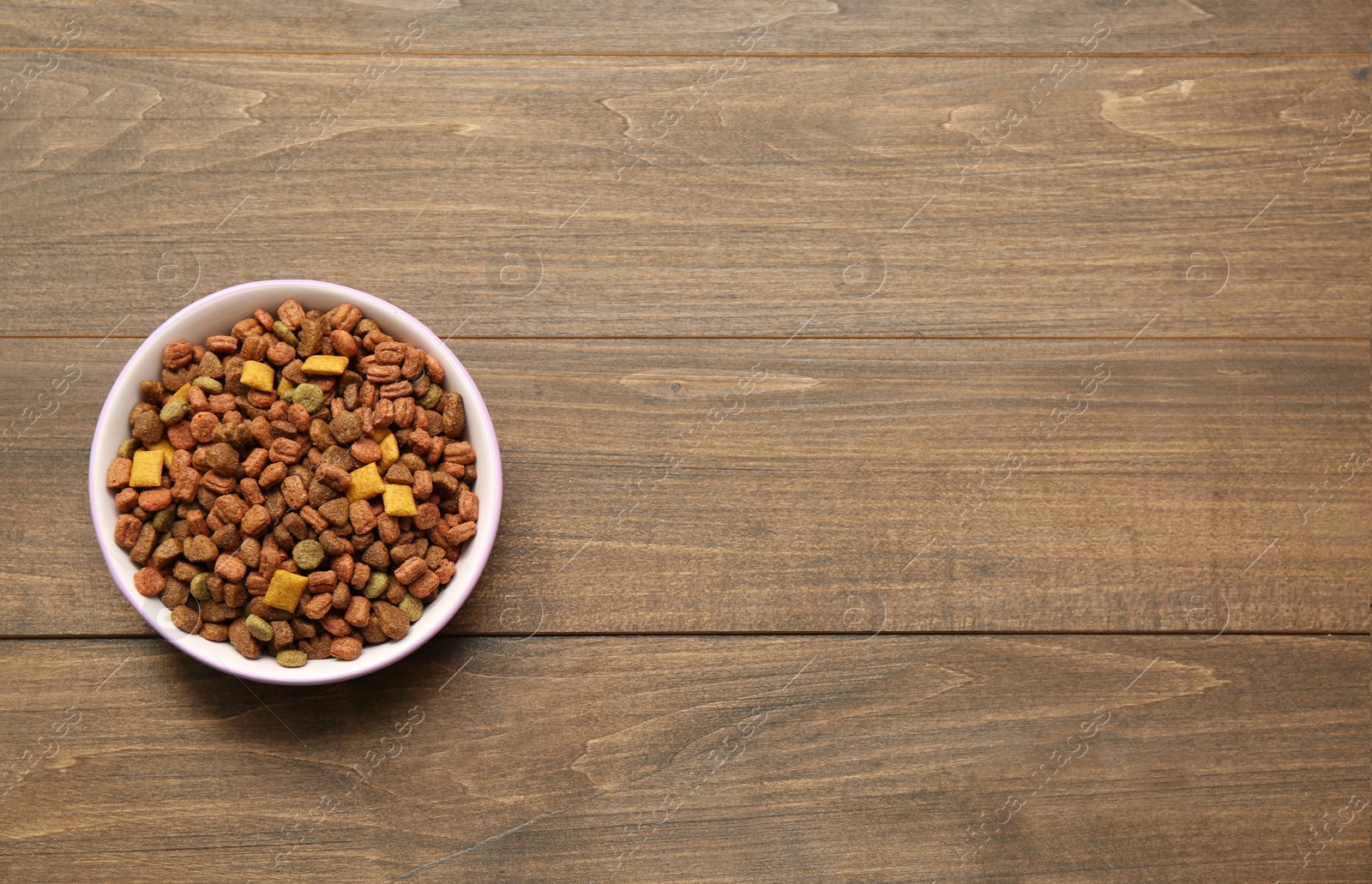 Photo of Dry food in pet bowl on wooden background, top view. Space for text