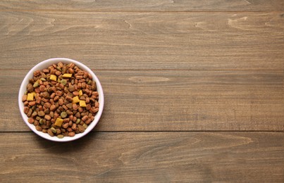 Photo of Dry food in pet bowl on wooden background, top view. Space for text