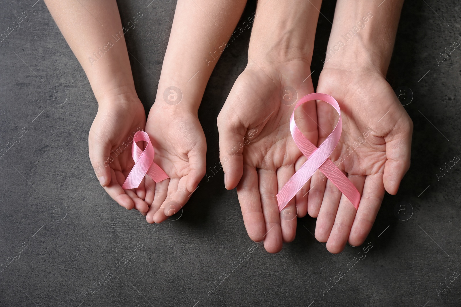 Photo of Woman and girl holding pink ribbons on grey background, top view. Breast cancer awareness