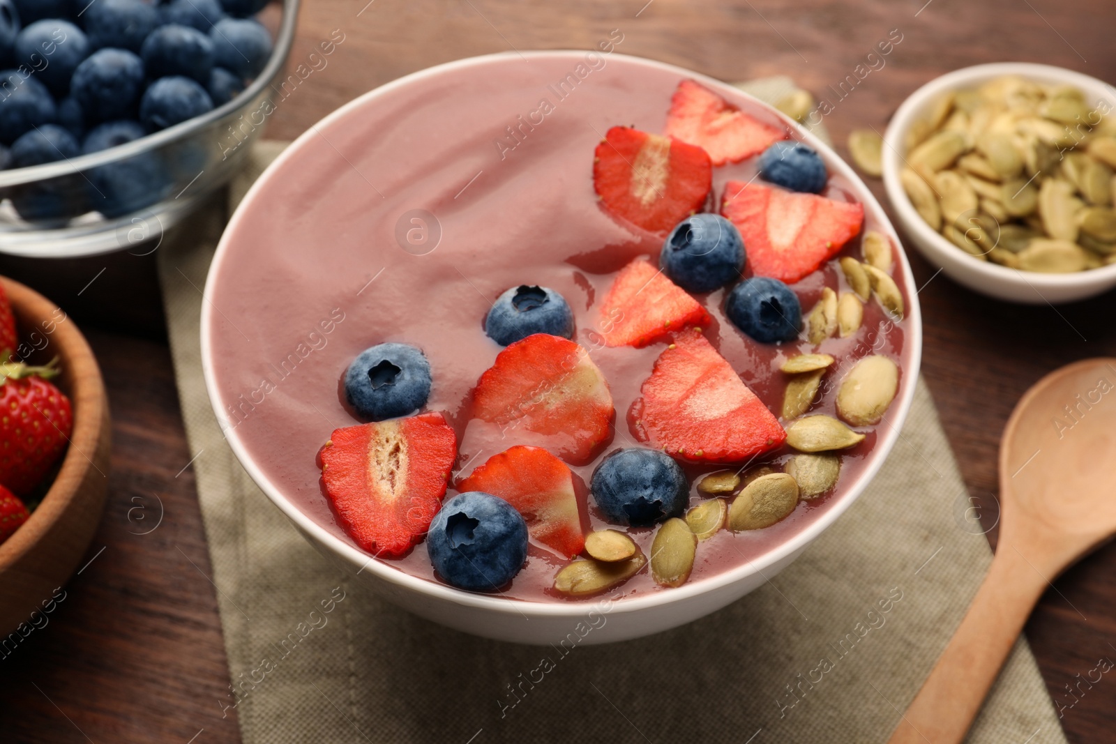 Photo of Bowl of delicious smoothie with fresh blueberries, strawberries and pumpkin seeds on wooden table, closeup