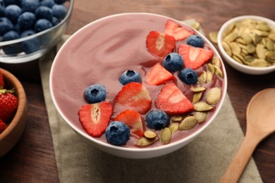 Photo of Bowl of delicious smoothie with fresh blueberries, strawberries and pumpkin seeds on wooden table, closeup