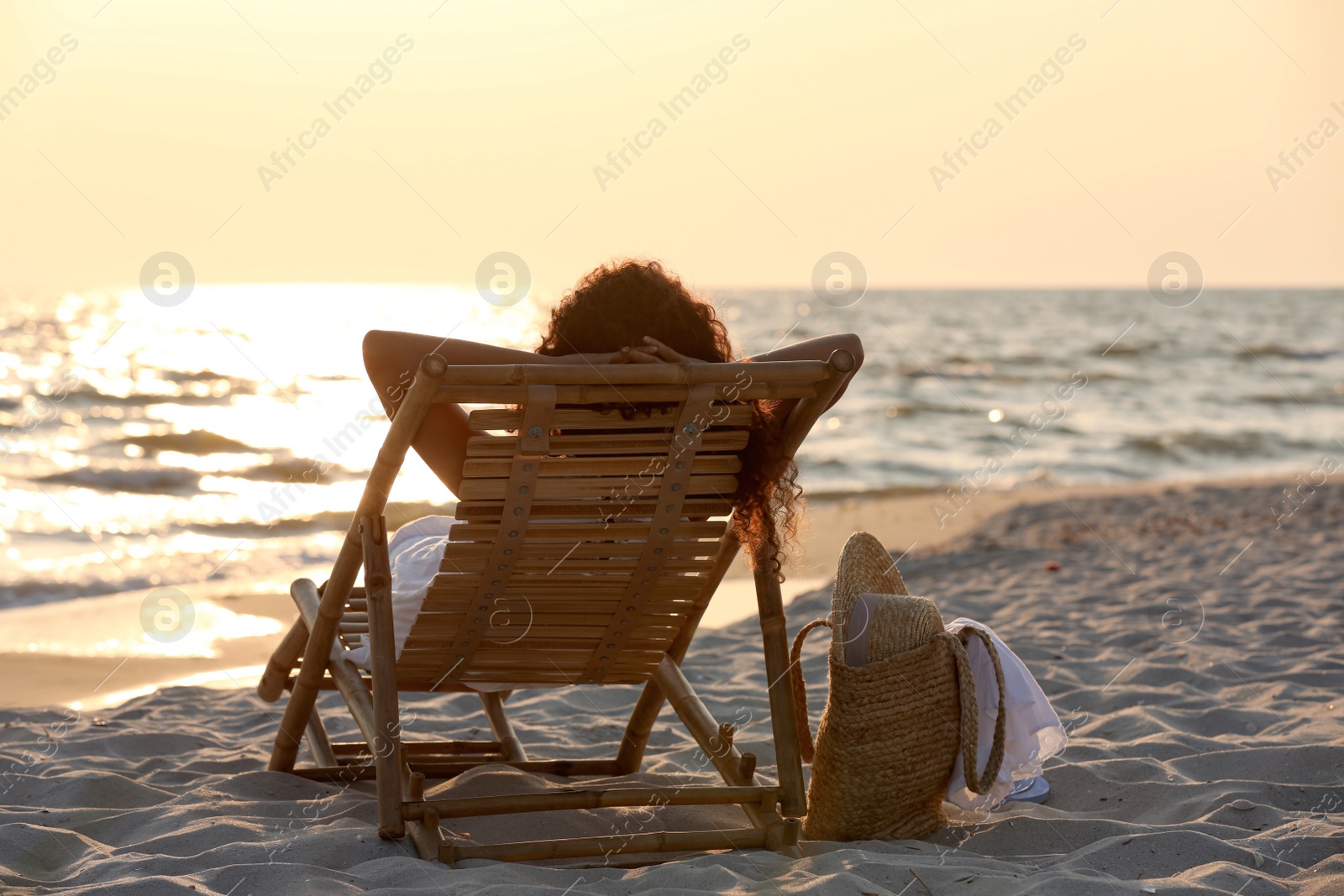 Photo of Woman resting in wooden sunbed on tropical beach at sunset