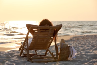 Woman resting in wooden sunbed on tropical beach at sunset