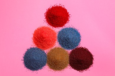 Photo of Heaps of different bright food coloring on pink background, flat lay