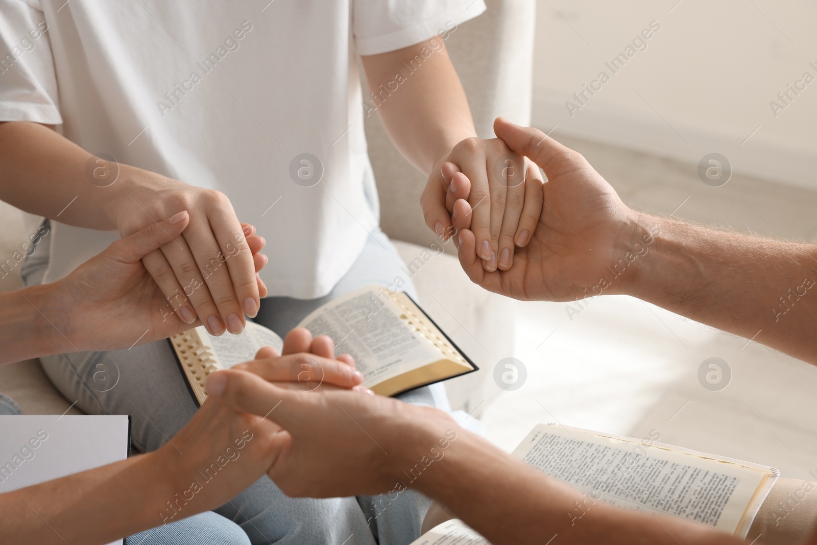 Photo of Group of religious people with Bibles holding hands and praying together indoors, closeup