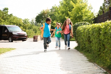 Photo of Cute little children with backpacks running outdoors. Elementary school