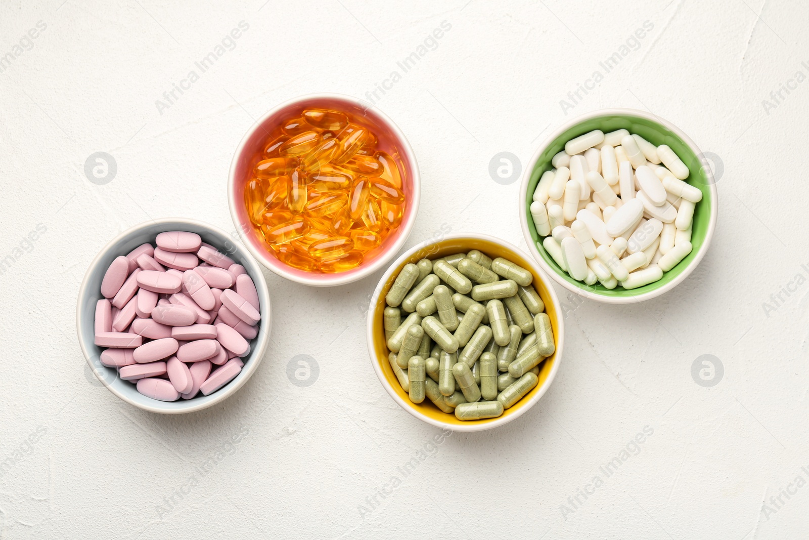 Photo of Different vitamin capsules in bowls on white wooden table, flat lay