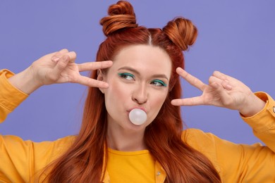 Photo of Portrait of beautiful woman with bright makeup blowing bubble gum and gesturing on violet background