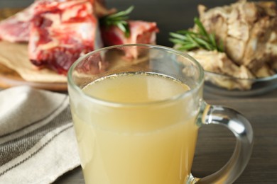 Photo of Glass cup with delicious bone broth on table, closeup
