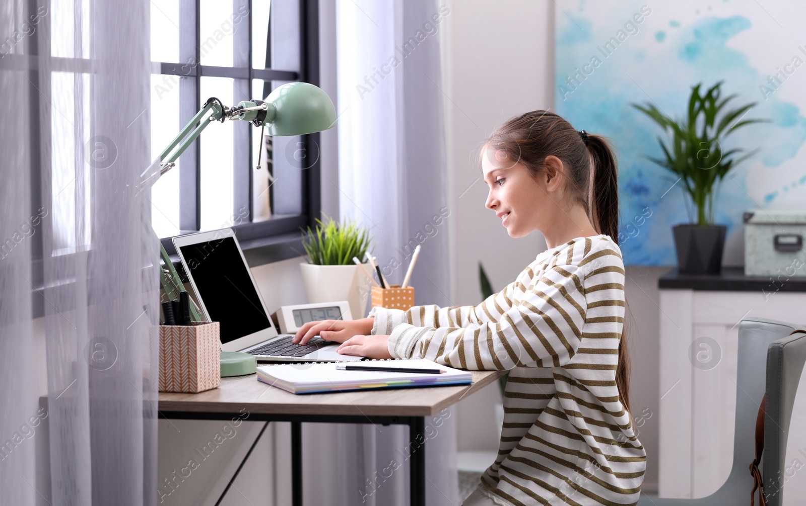 Photo of Pretty preteen girl doing homework at table in room