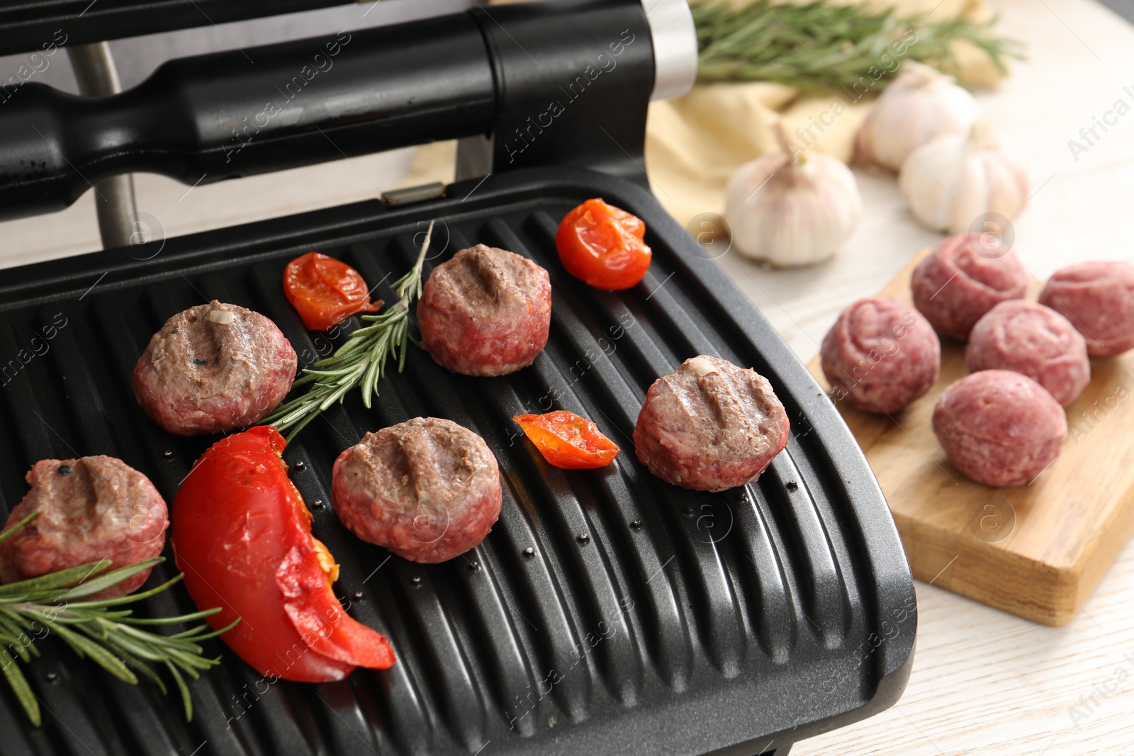 Photo of Electric grill with vegetables, meat balls and rosemary on table, closeup