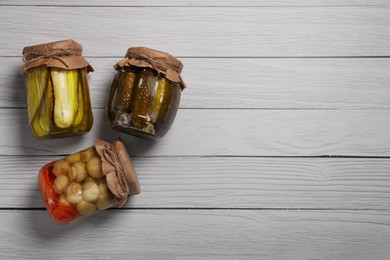 Jars with pickled vegetables on white wooden table, flat lay. Space for text